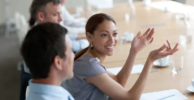 Business meeting scene with a smiling woman gesturing at a table